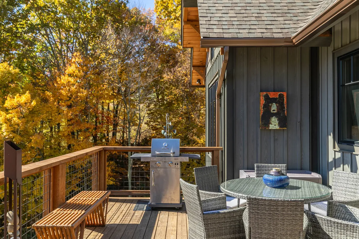A relaxed exterior shot of a grill and outdoor dining table set amid lush foliage, suggesting a space designed for alfresco meals and social gatherings in nature.