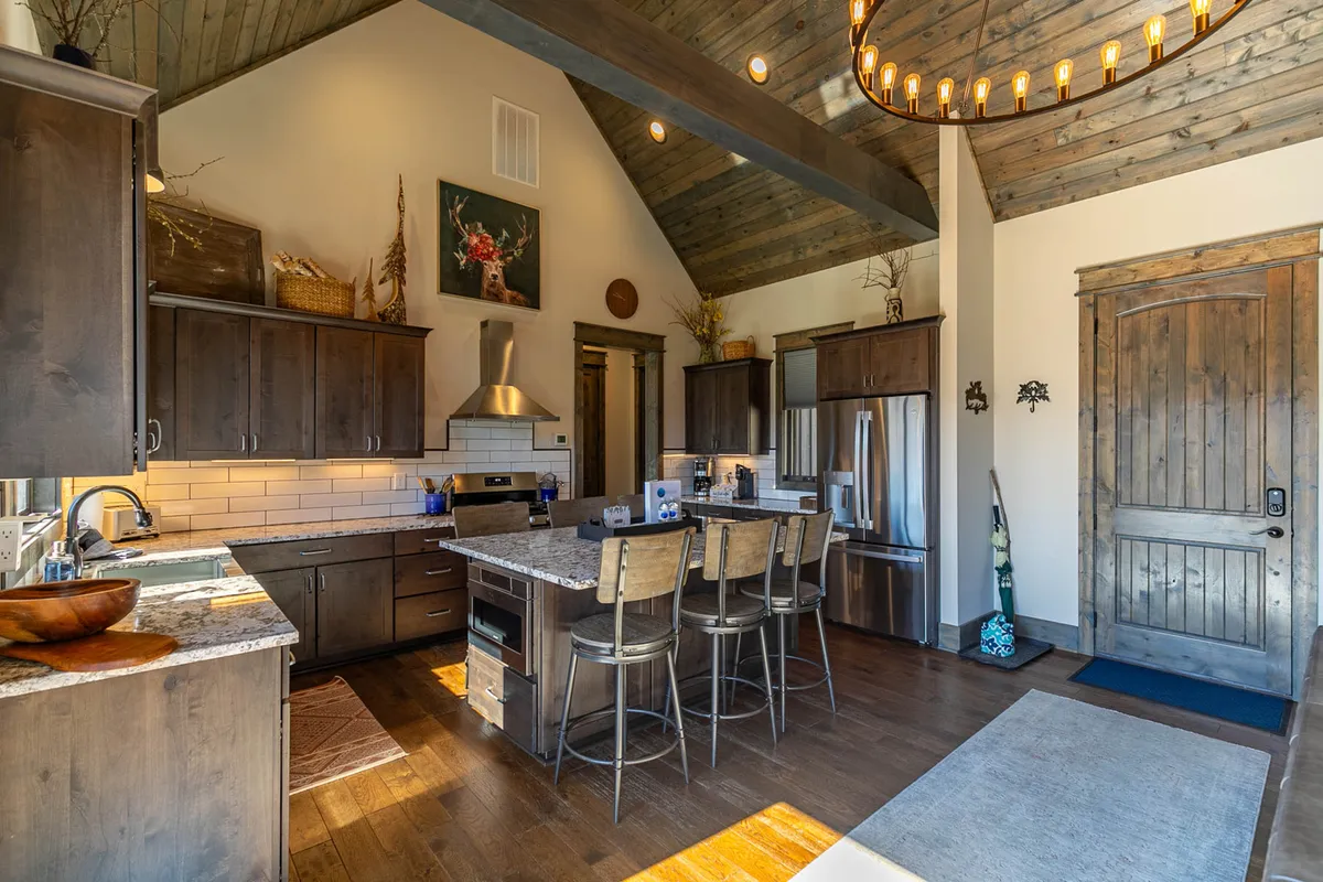 An inviting kitchen with a large central island, elegant chandelier, extensive wooden cabinetry, and polished granite countertops. The space is set up for cooking, entertaining, and family gatherings, embodying the heart-of-the-home ambiance.