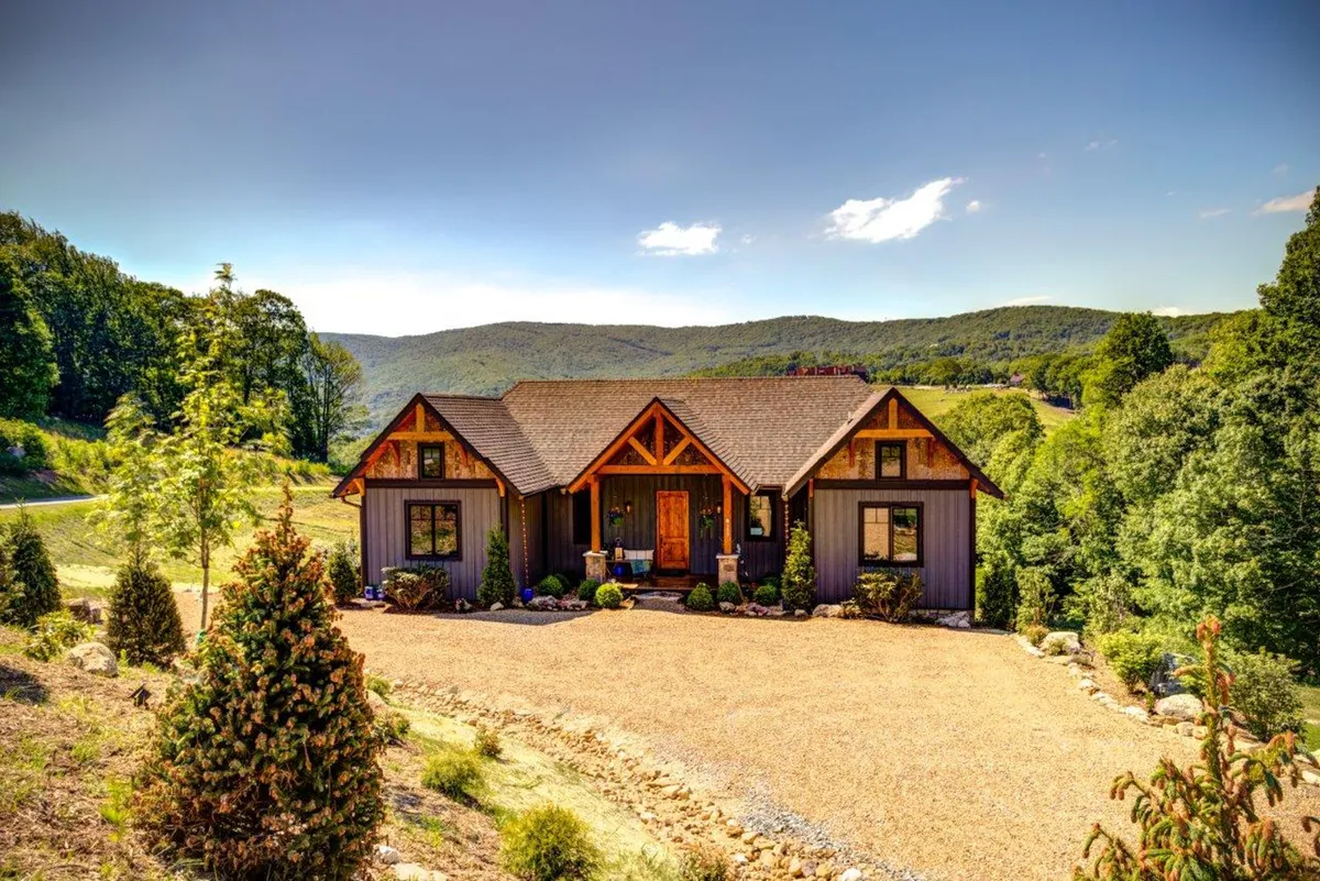 A welcoming front porch with unique roof design, surrounded by lush landscaping and offering views of the mountains. The space features ample seating, perfect for enjoying morning coffee or evening gatherings under the open sky.