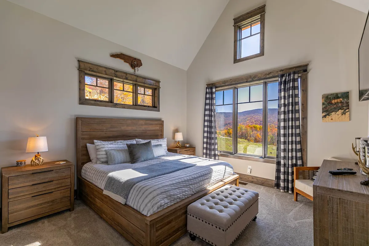 A tranquil bedroom featuring a plush bed with soft linens, a nightstand, decorative art, and a large window framing mountain views. The space exudes peacefulness and invites relaxation, ideal for highlighting the restful atmosphere of a King suite.