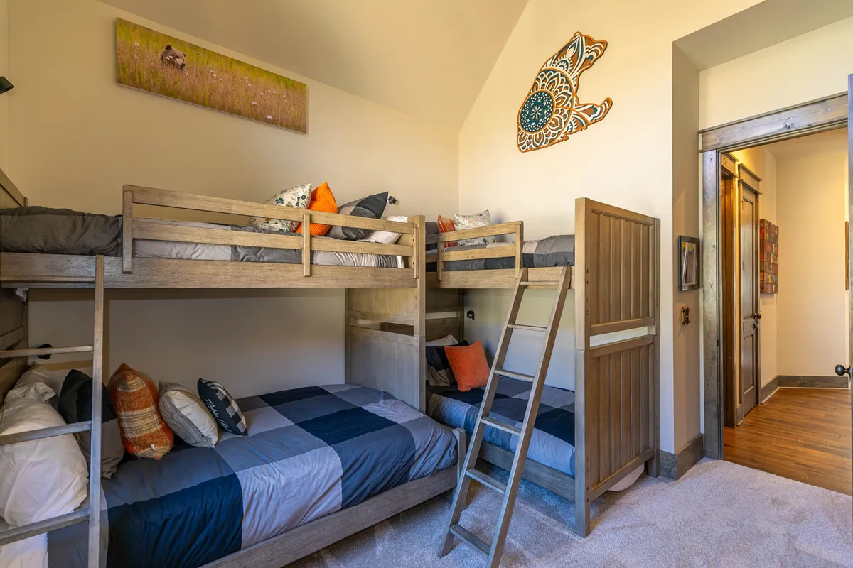 A playful bunk room with colorful pillows, built-in bunk beds (including a larger lower bunk), and cheerful wall art. The room is bright and kid-friendly, perfect for families or groups of children.