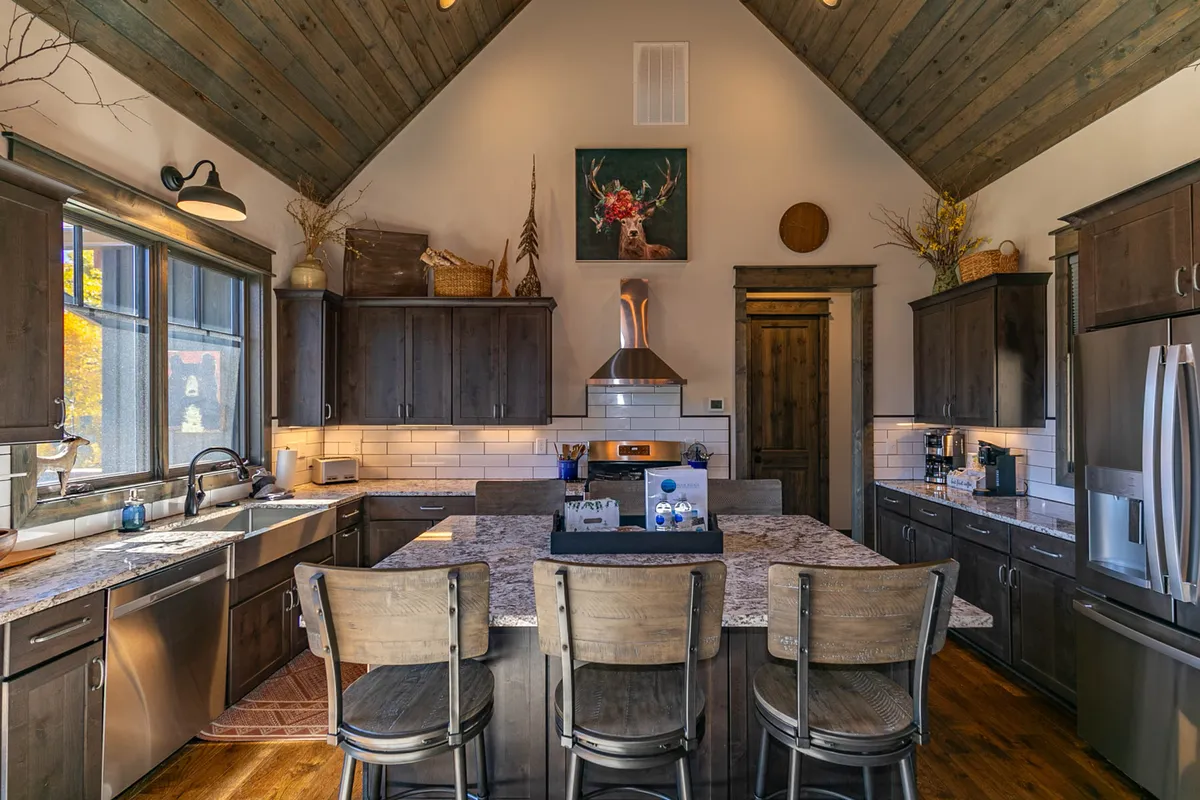 A spacious kitchen featuring an oversized island with ample seating, gleaming stainless-steel appliances, wooden cabinetry, and inviting lighting. The island anchors the space as a hub for food prep and socializing, while the appliances and countertop space signal a chef-ready environment.