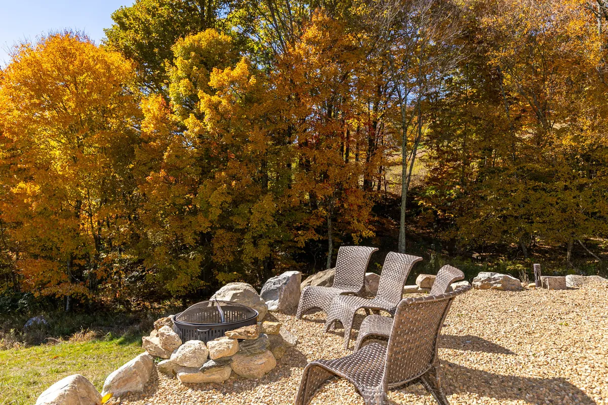 The image features a cozy fire pit set amidst rock seating and surrounded by colorful autumn trees. The inviting circular arrangement encourages gatherings and relaxation after active days outdoors.